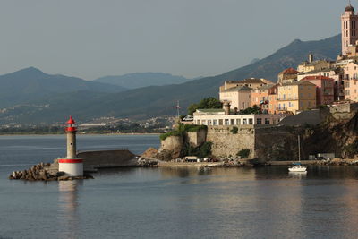 Lighthouse by sea and buildings against sky