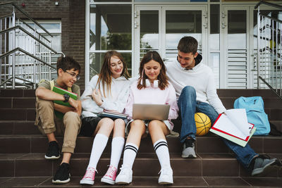 Girl doing homework over laptop by friends sitting on steps at school