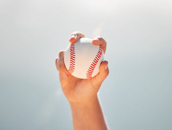 Cropped hand holding baseball against clear sky