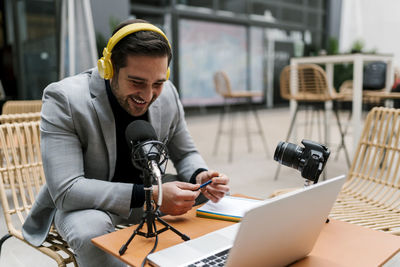 Smiling businessman using microphone while vlogging at cafe