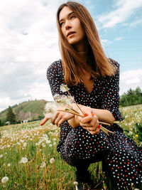 Beautiful young woman holding camera on field against sky