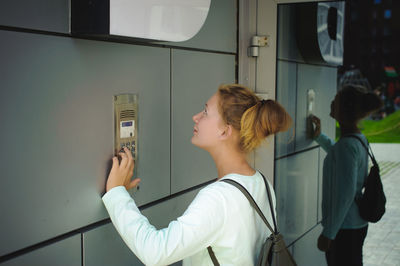 Side view of young woman using intercom
