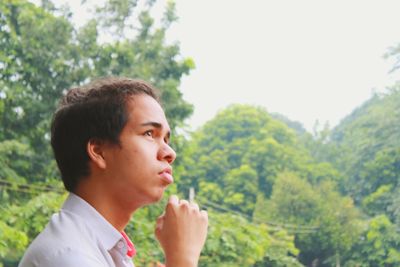 Portrait of young man looking away against trees