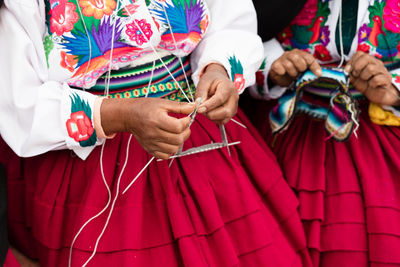 Midsection of women wearing traditional clothing knitting wool