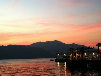 Silhouette river by illuminated mountains against sky at sunset