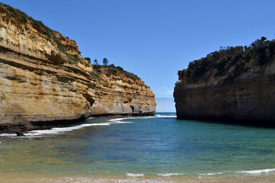 Rock formations by sea against clear blue sky