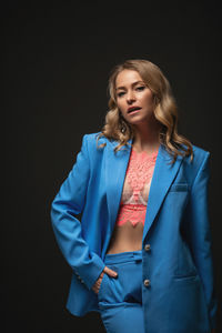 Portrait of young woman standing against black background