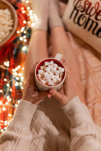 Cup of cocoa or coffee drink with marshmallows in female holding hands over the legs of woman