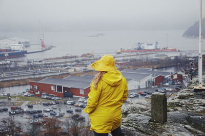 Rear view of woman in yellow warm clothing standing against sky