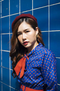 Portrait of young woman standing against blue wall