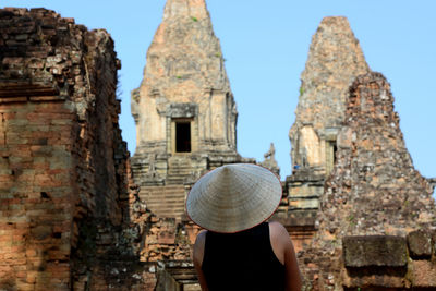 Rear view of person wearing asian style conical hat against historic temple