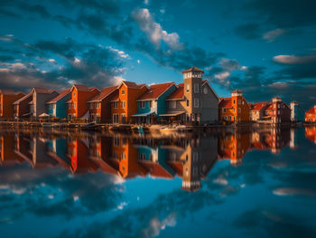 Reflection of illuminated buildings in sea against sky at dusk