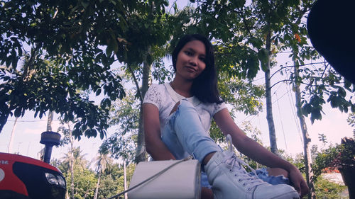 Portrait of smiling young woman sitting against trees