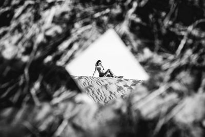 Reflection of woman sitting on sand in mirror