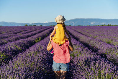 Mother piggybacking little daughter in vast summer lavender field