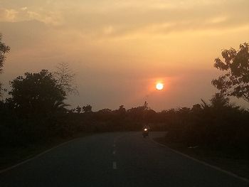 Road by silhouette trees against sky during sunset