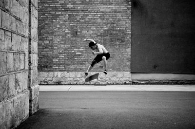 Side view of man skateboarding on street against brick wall