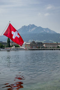 Red flag by lake against sky in city