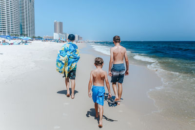 Boys walking down beach against sky