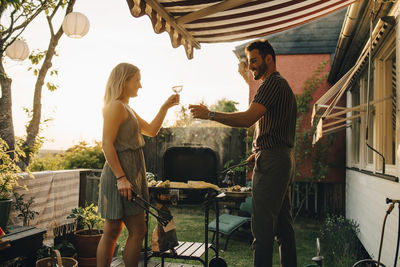 Happy friends raising toast while preparing food on barbecue grill in dinner party