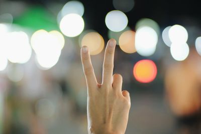 Cropped hand of woman gesturing peace sign against lights at night