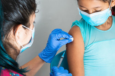 Children's nurse wiping blood with cotton wool after administering injection in brown girl's arm.