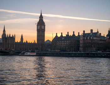 River and buildings against sky at sunset