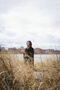 Thoughtful senior woman looking away while standing against cloudy sky in city