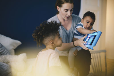 Mother carrying son while showing digital tablet to boy at home