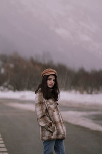 Portrait of young woman standing in park against sky during winter