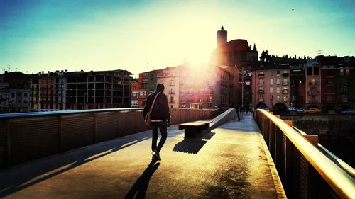 Men walking on bridge by buildings on sunny day