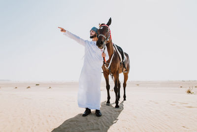 Man pointing while standing with horse against sky