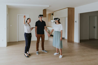 Smiling couple wearing virtual reality simulators while standing by real estate agent on floor