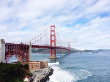 Suspension bridge over sea against cloudy sky