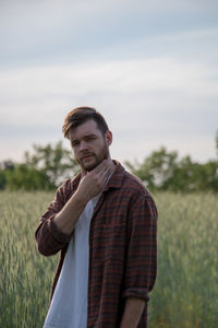 Portrait of young man standing on field against sky