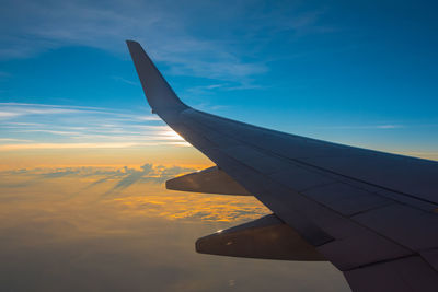 Airplane wing against sky during sunset