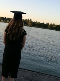 Rear view of woman standing by river against sky