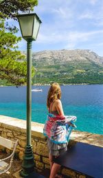 Woman looking at sea while standing by street light