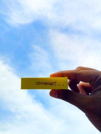 Low angle view of hand holding sign against sky