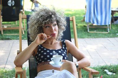 Young woman drinking glass while sitting on chair