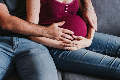 Midsection of pregnant woman sitting with male partner on sofa at home