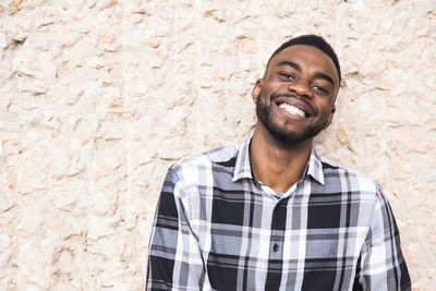 Portrait of happy young man leaning against wall