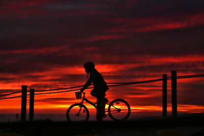 Silhouette man with bicycle against sky during sunset