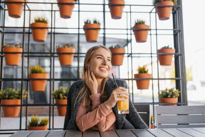 The trend of a healthy lifestyle is a young woman drinking orange juice at a table in a summer cafe.