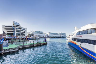 Boats in canal by city against clear blue sky