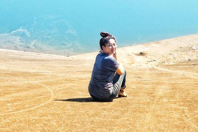 Full length rear view portrait of woman sitting at beach during summer