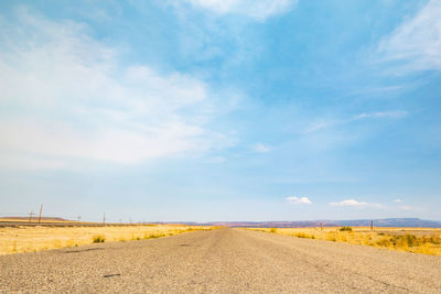 Empty road amidst field against sky