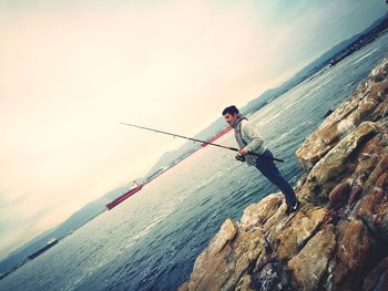 Man standing on fishing net by sea against sky