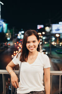 Portrait of smiling woman standing in city at night