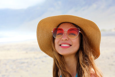 Portrait of smiling young woman wearing sunglasses and hat at beach